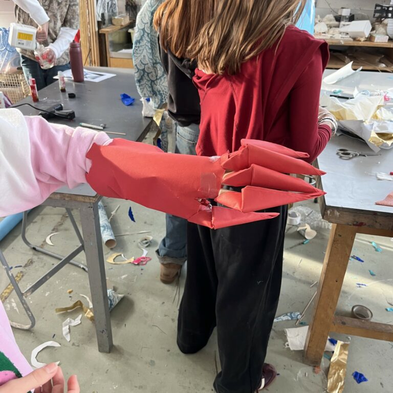 A student models a 'claw' and cuff made from red paper