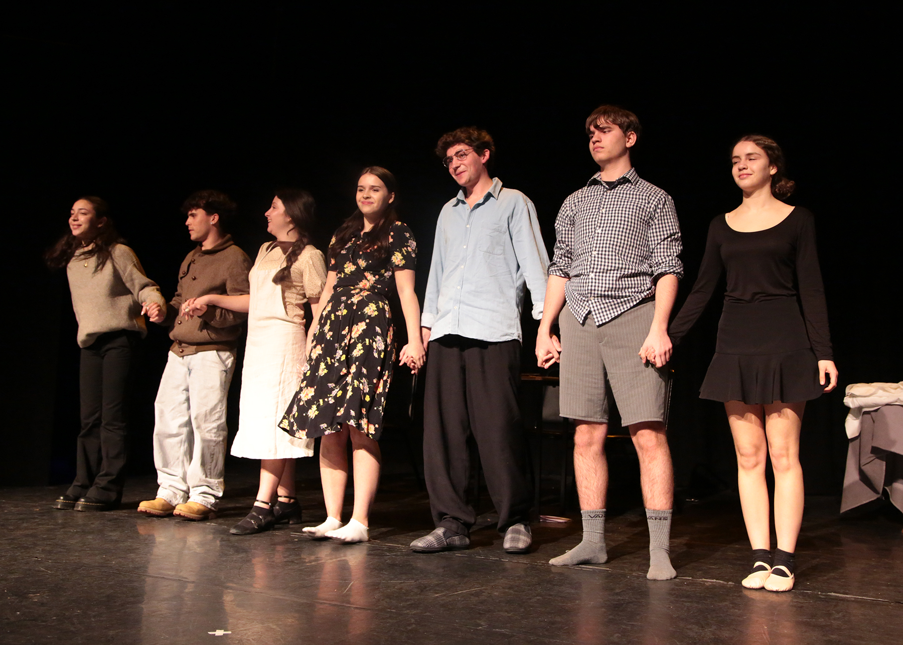 Students standing in a line hold hands on stage