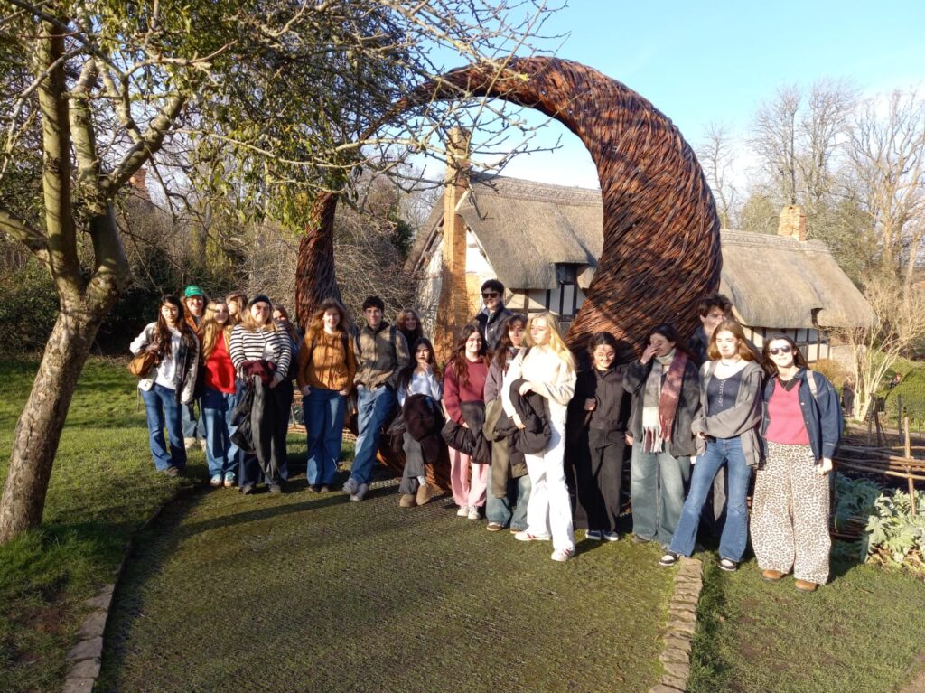 A group of Sixth Form students stand in a line in front of a thatched-roof cottage, the childhood home of Anne Hathaway, who went on to marry William Shakespeare