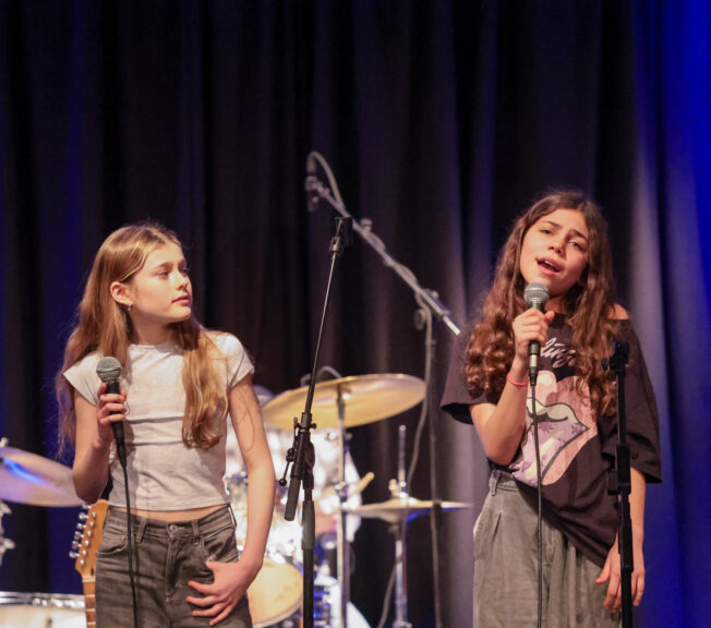 Two female students hold microphones to sing on stage
