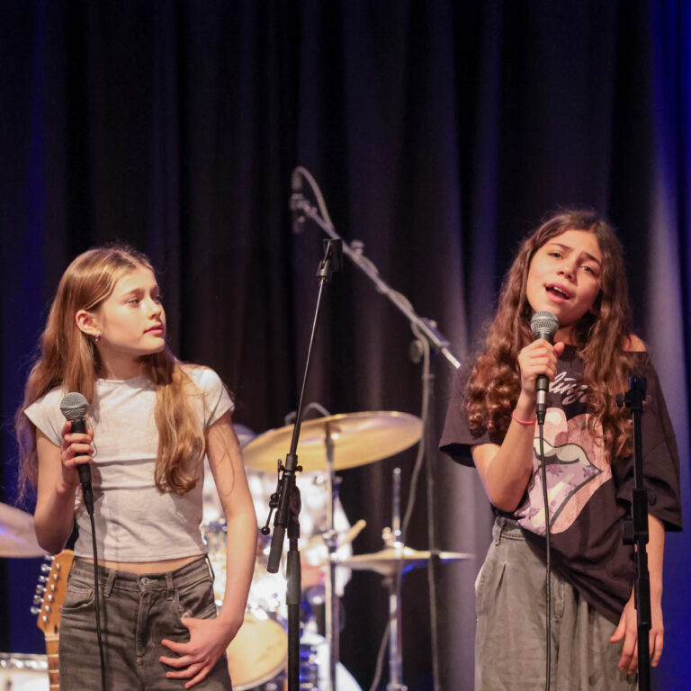 Two female students hold microphones to sing on stage
