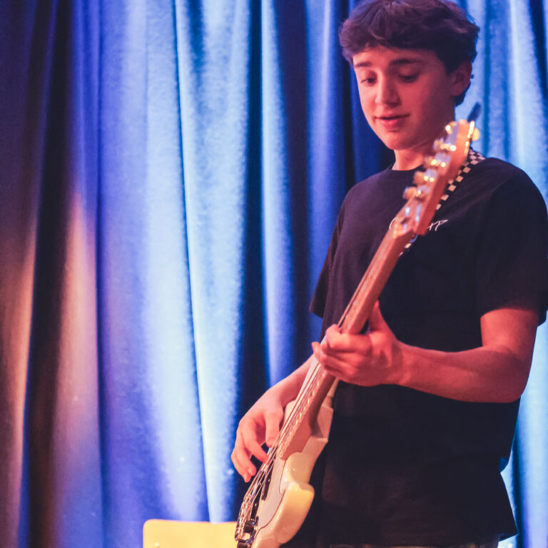 A male student plays an electric guitar on stage