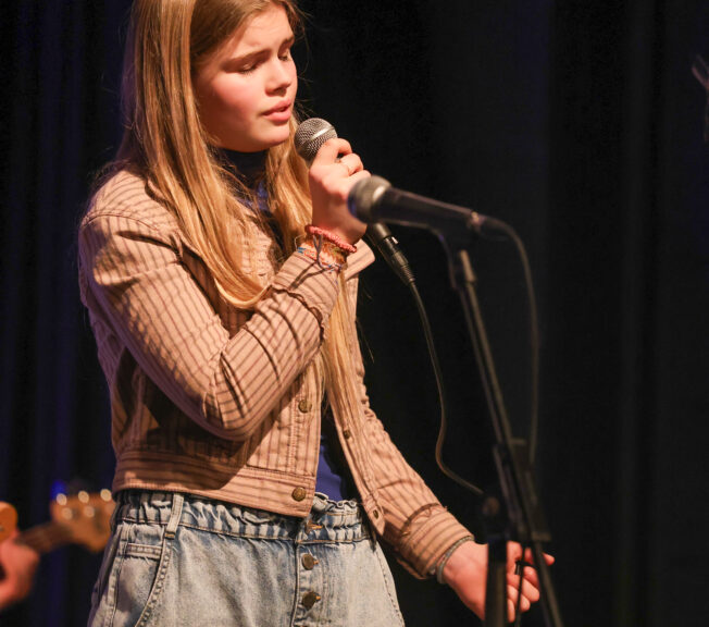 A female student sings into a microphone on stage during a concert