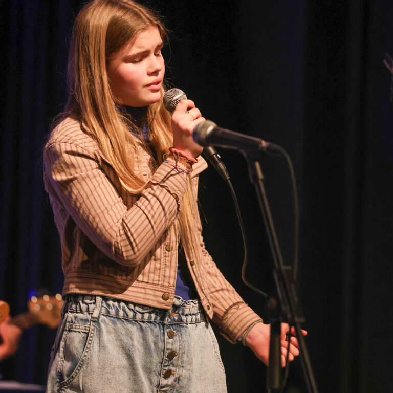 A female student sings into a microphone on stage during a concert