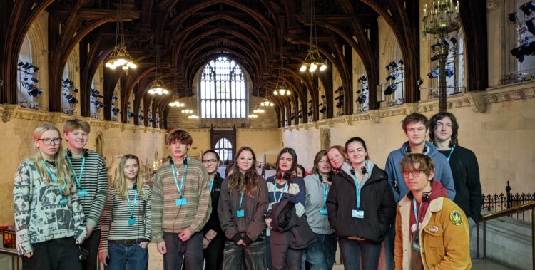 A line of Sixth Form students pose for a picture in a grand hall, featuring an arched wooden roof and stained glass windows.