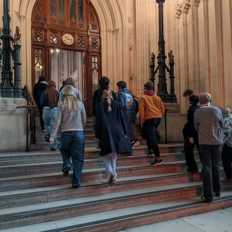 A group of Sixth Form students from The King Alfred School, North London, walk up stone steps to an ornate wooden door at the Houses of Parliament, UK