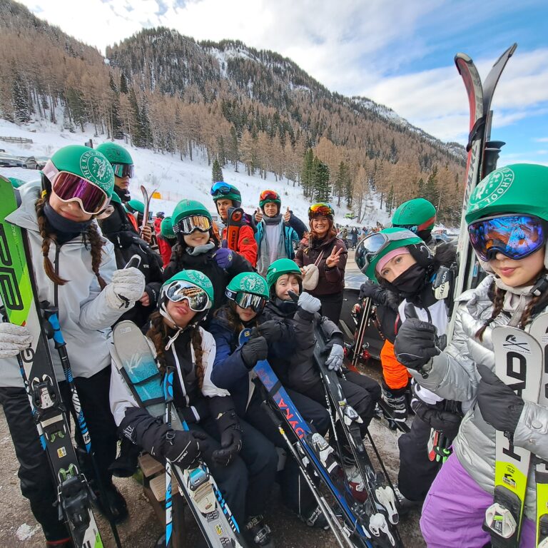 A group of students and teachers from The King Alfred School, North London, post with their skis in front of a mountain