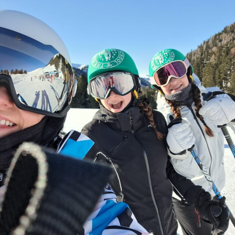 Three smiling students have fun on a ski slope