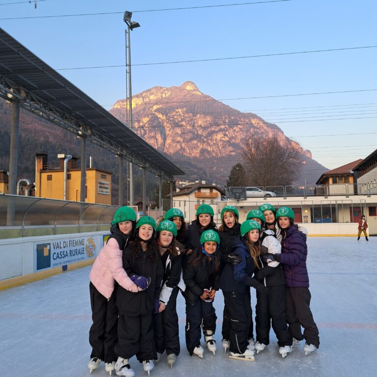 A group of female students pose on an outdoor ice rink, with a mountain scene behind them