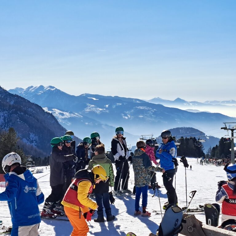 A group of students and teachers pictured on top of a snowy mountain in a ski resort
