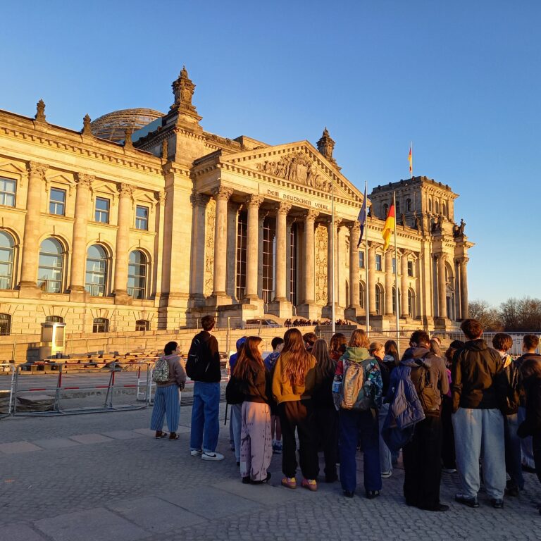 A large group of students look up at a grand old building drenched in sunlight in Berlin