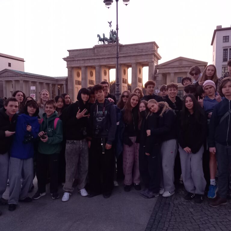 A large group of students pose at sunrise in front of the Brandenburg Gate in Berlin