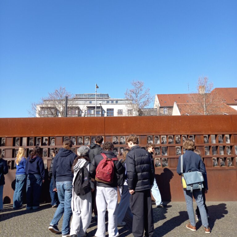 A group of students from The King Alfred School look at pictures of people on a war memorial wall in Berlin