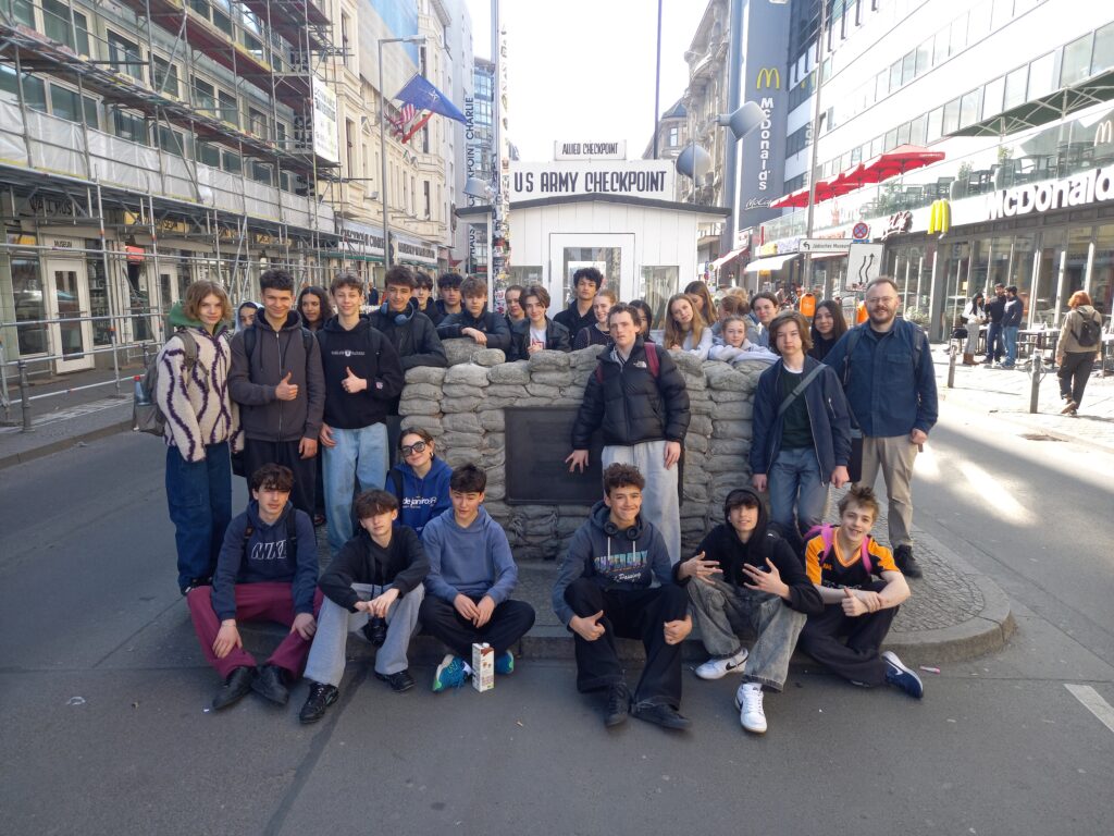 A group of students from The King Alfred School pose in front of Checkpoint Charlie in a Berlin street