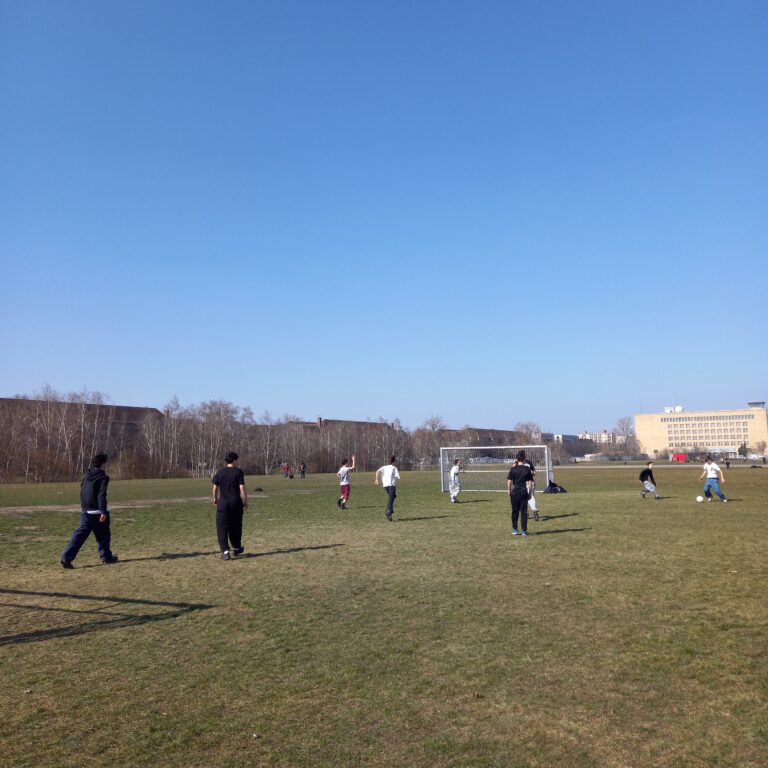A group of student walk across a vast field in Berlin, with a bright blue sky behind them