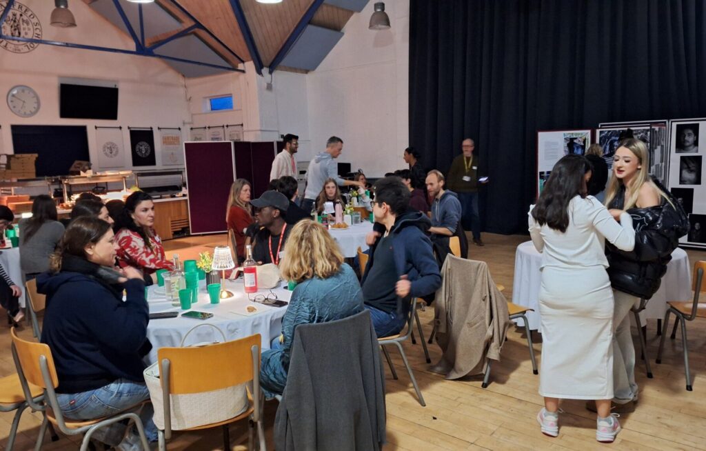 Parents, teachers and staff sit at round tables in a school hall