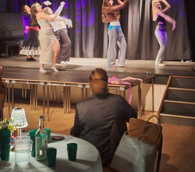 Female student perform bellydancing moves on a stage whilst a parent watches on