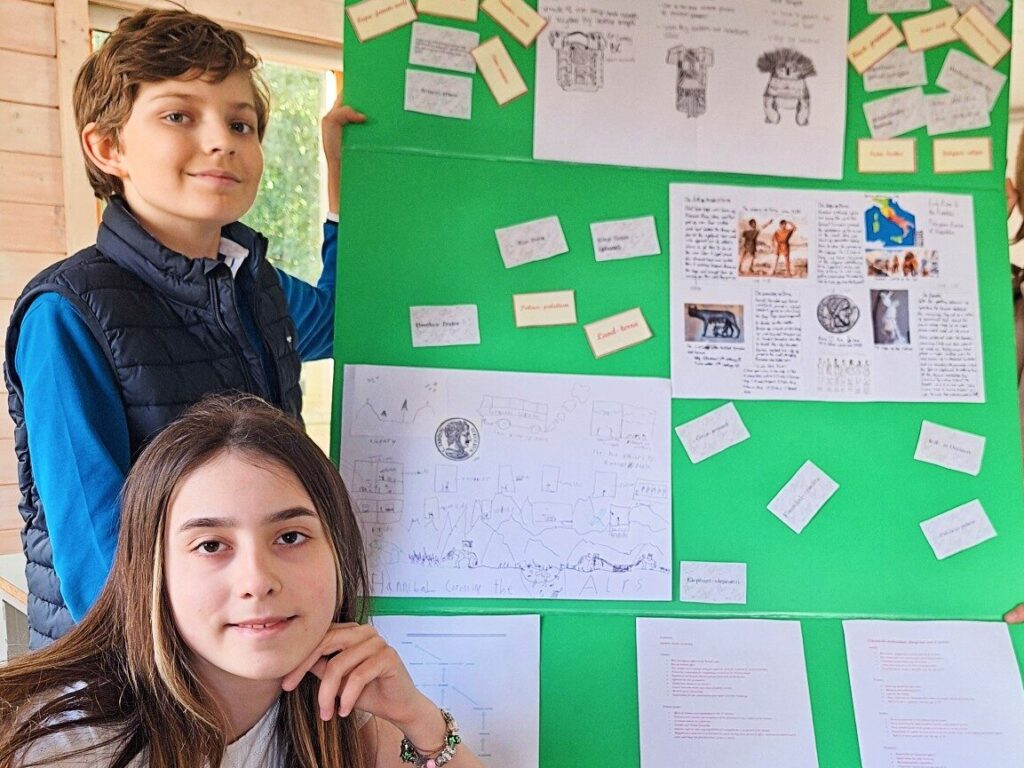 A group of three Year 8 students from The King Alfred School hold up a display of their work on Ancient Rome