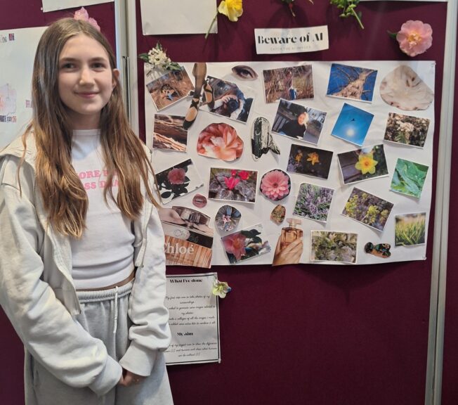A young female student poses next to a display of her work on digital manipulation of images using AI