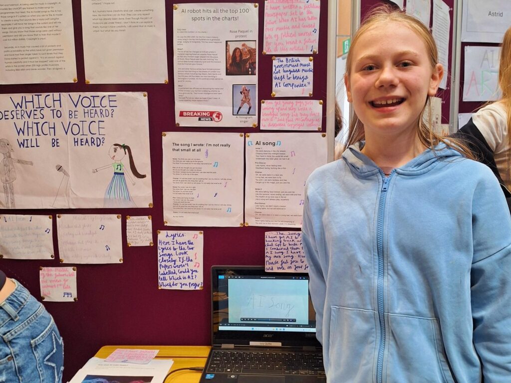 A young female student stands proudly next to a display of her work on the ethics and value of AI in music