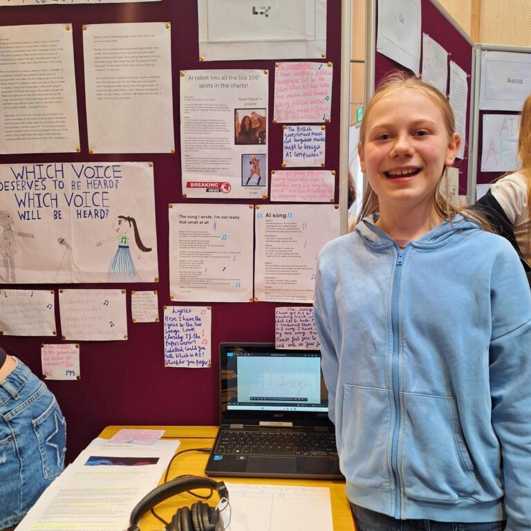 A young female student stands proudly next to a display of her work on the ethics and value of AI in music