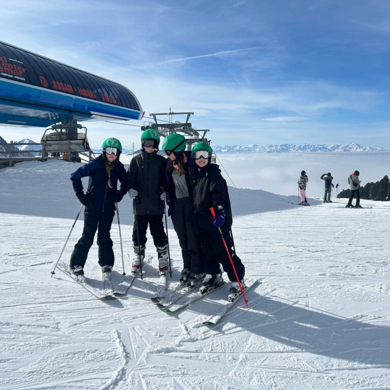 Students pose on skis with a ski resort behind them