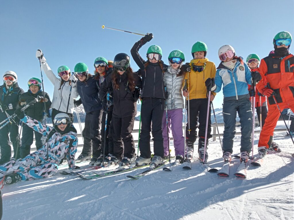 Students wearing skis and snowsuits pose in a line on a snowy mountain