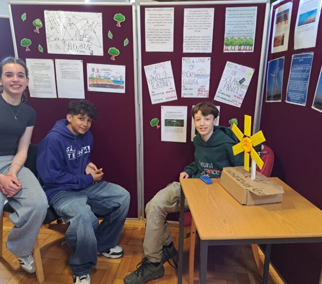 Three students sit in front of a display of their work on restoring the natural balance
