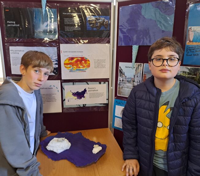 Two students pose in front of a display of their work on permafrost melting