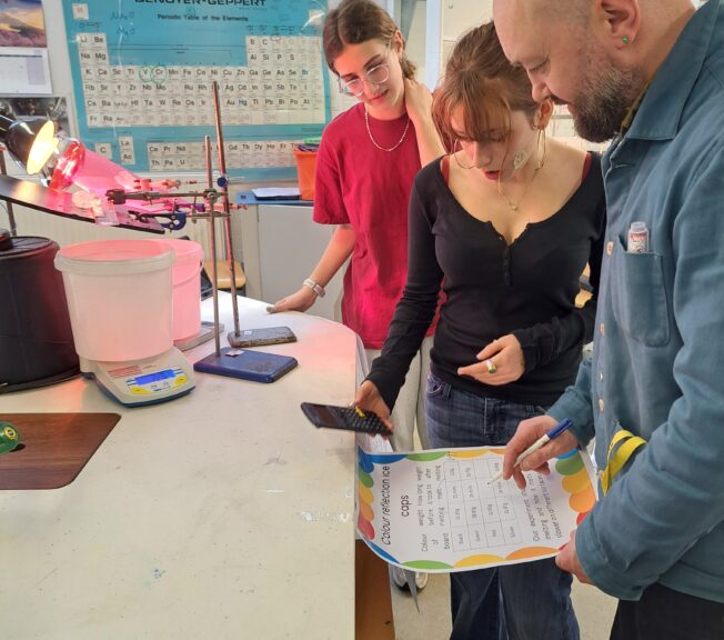 Two students and a teacher consult a clipboard in a science lab as they recreating icecap melting