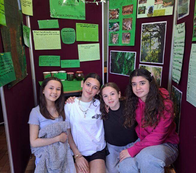 Four female students kneel in front of a display of their work on the Amazon