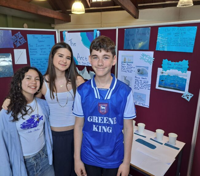 Three young students pose in front of a display of their work on the Arctic