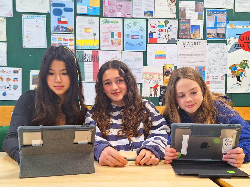 Three female students working at a desk in a Modern Foreign Languages lesson, with displays of work on the wall behind them
