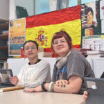 Two male and two female students sit at desks in a Modern Foreign Languages classroom, looking at iPads and the front of the room. There are displays of work and a large Spanish flag in the background.