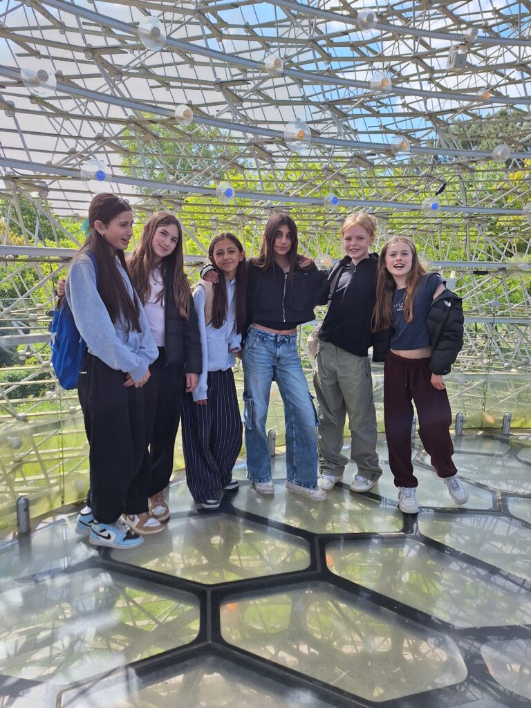 A group of female students pose inside a metal and glass structure at Kew Gardens