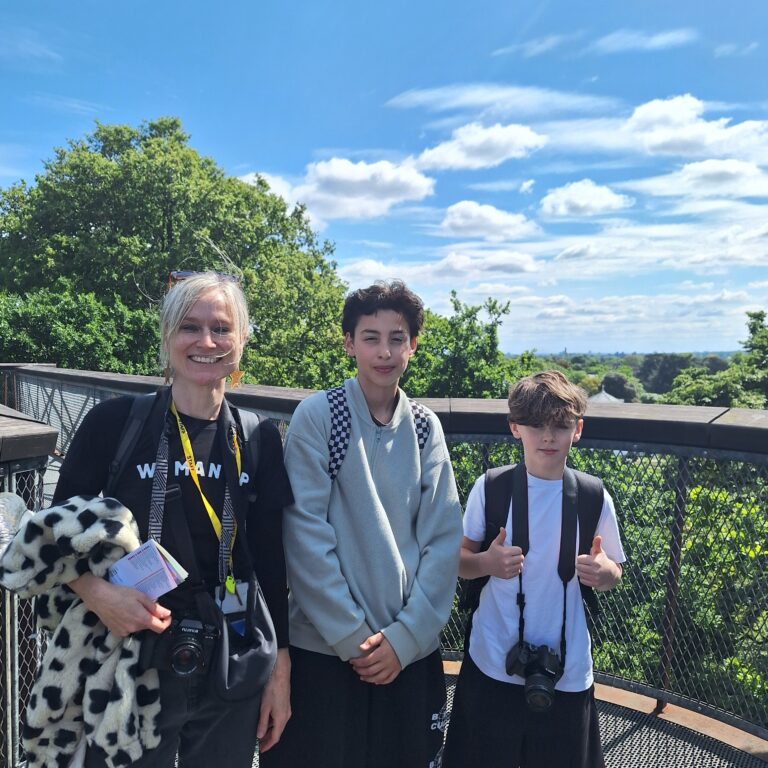 Two students and a teacher pose for a photograph on a treetop walkway at Kew Gardens