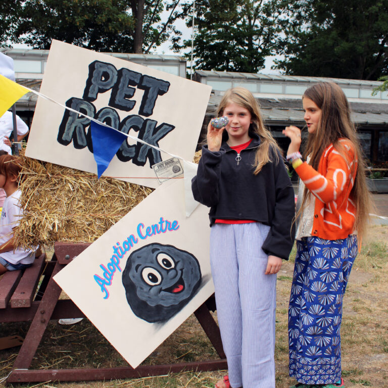 Two female students pose holding small stones in front of a sign that reads 'Pet Rock Adoption Centre'