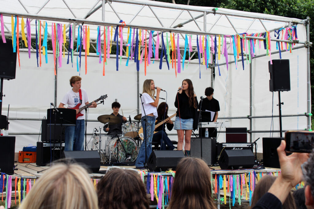 A student band performs on stage decorated with multicoloured streamers on The King Alfred School field