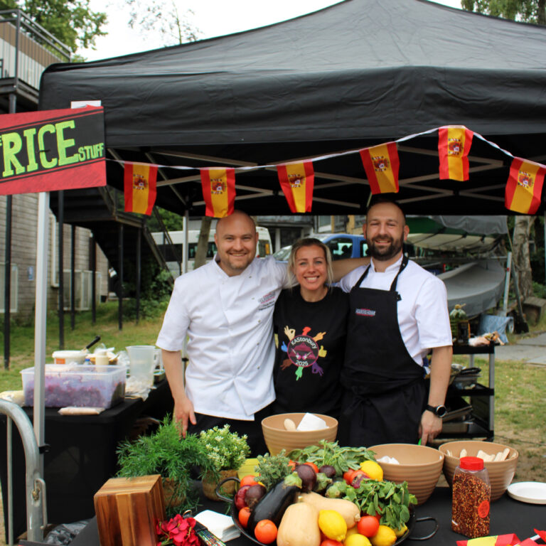 Three kitchen staff smile with their arms around one another on a rice box and falafal food stall
