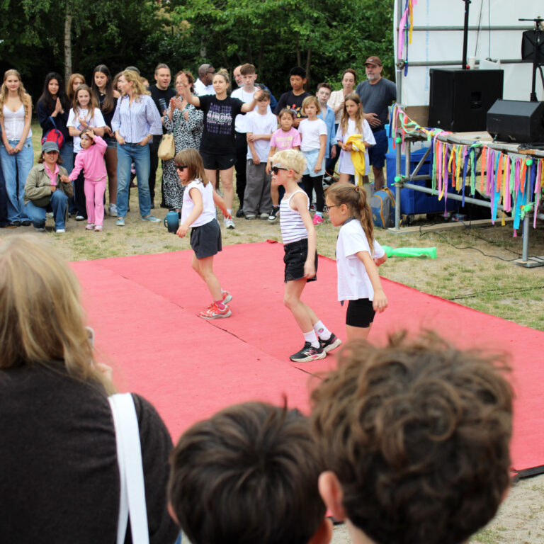 Students perform dressed in black shorts, white tees and black sunglasses as parents watch on