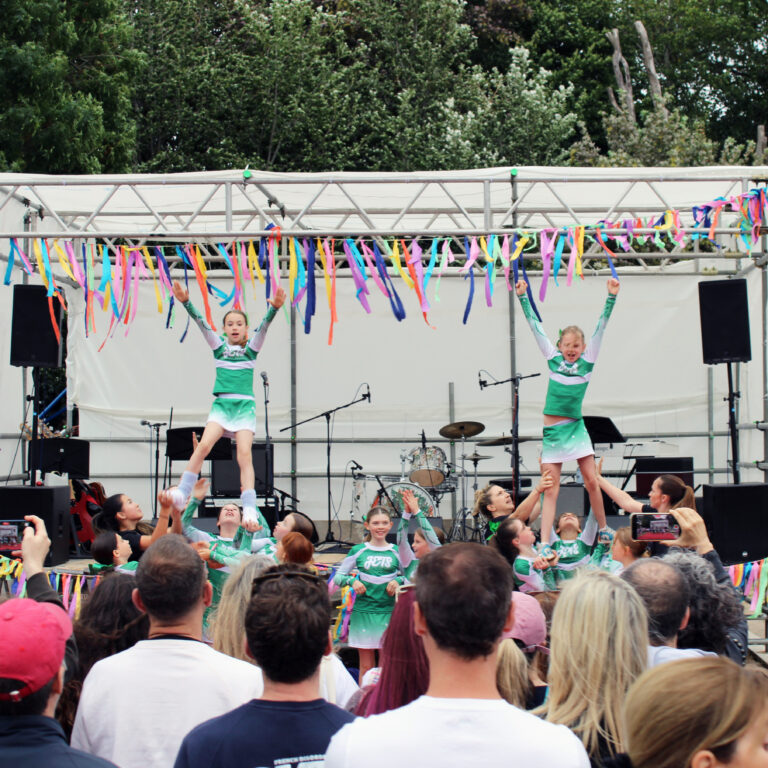 Cheerleaders perform to a crowd in front of a stage decorated with colourful streamers