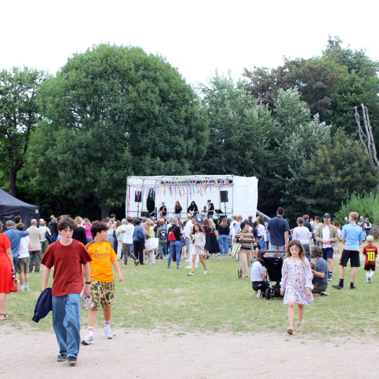 The crowd on The King Alfred School field during KAStonbury 2025, with students performing on a stage in the distance