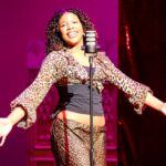 A female student wearing a leopard print outfit holds out her hands and smiles on stage