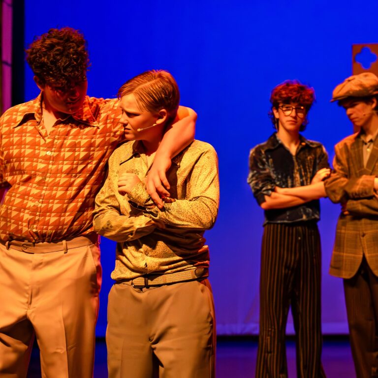 Male students dressed as mobsters stand on stage during a performance of Sister Act Jr