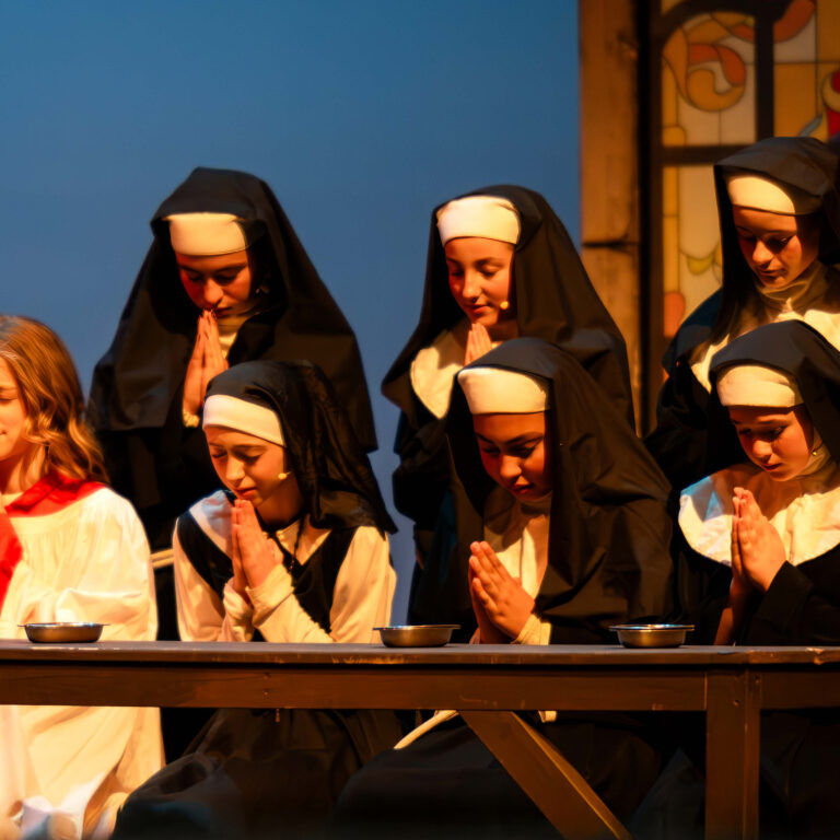 Students dressed as nuns and a choir boy pray on stage during The King Alfred School's production of Sister Act Jr