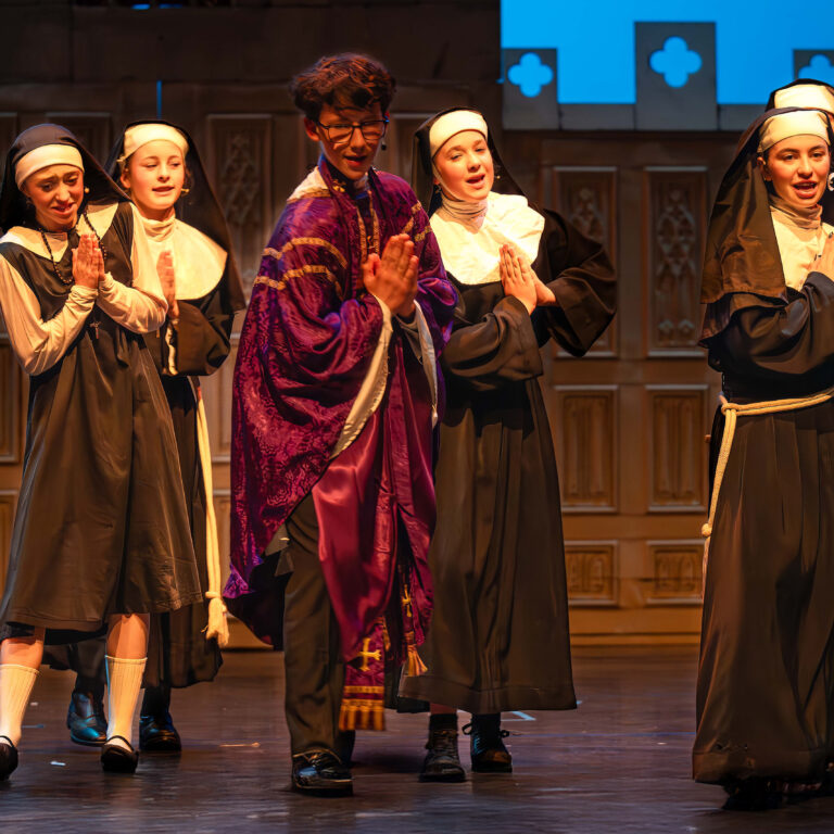 A male student dressed as a priest and four female students dressed as nuns dance on stage during a performance of Sister Act Jr
