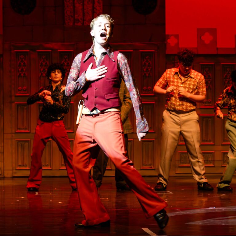 Male students dressed as mobsters dance on stage during a performance of Sister Act Jr