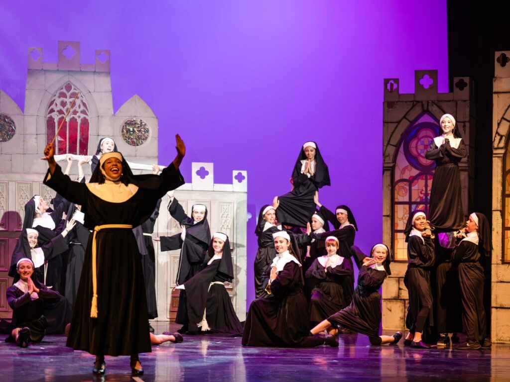 Students dressed as nuns perform on stage in a production of Sister Act Jr