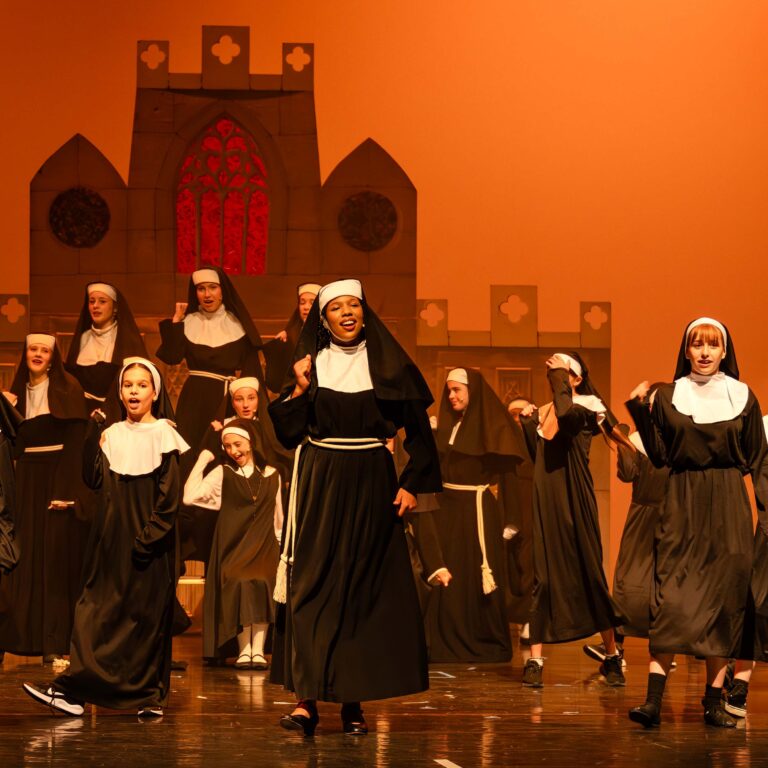 A group of students dressed as nuns sing on stage during a performance of Sister Act Jr