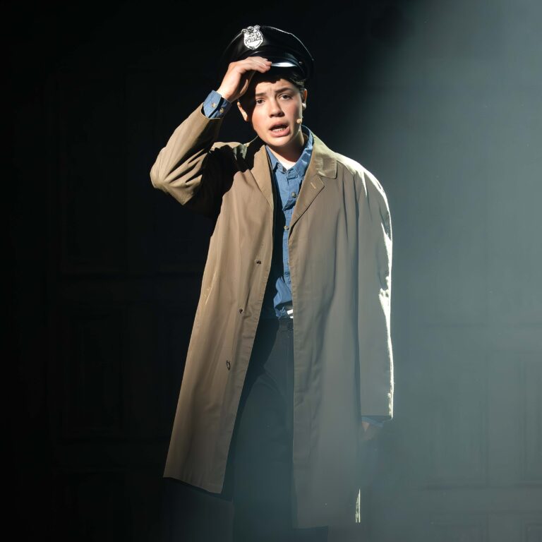 A male student dressed as a cop sings emotionally on a dark stage during The King Alfred School's production of Sister Act Jr